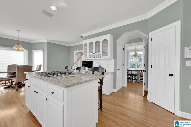 kitchen with glass insert cabinets, a kitchen breakfast bar, an inviting chandelier, light wood-style floors, and white cabinetry