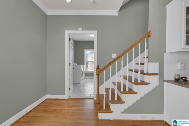 staircase with baseboards, wood finished floors, washer / dryer, and crown molding