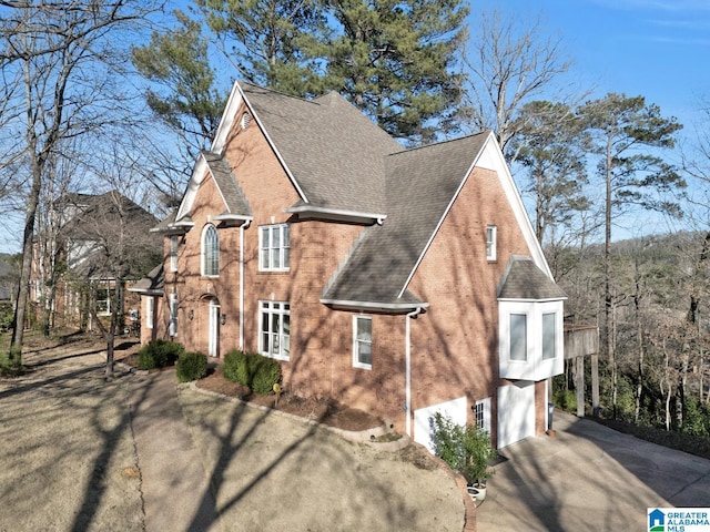 view of property exterior featuring a shingled roof, concrete driveway, and brick siding