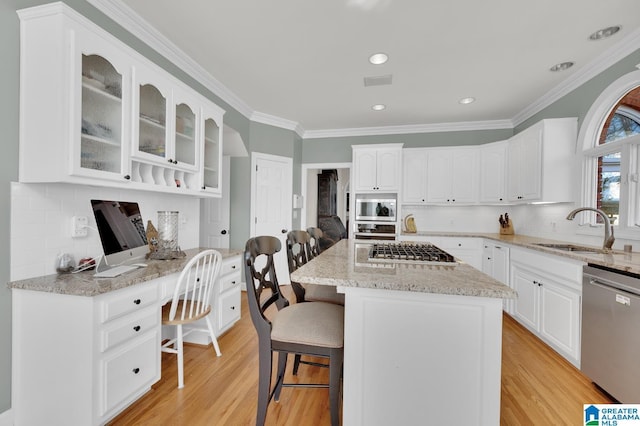 kitchen with a breakfast bar area, appliances with stainless steel finishes, glass insert cabinets, a sink, and light stone countertops