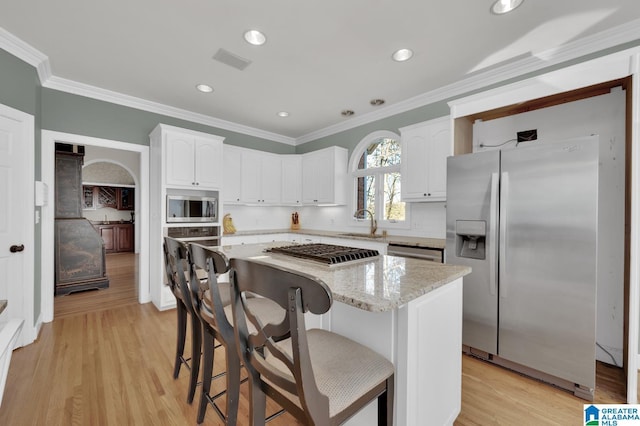 kitchen featuring appliances with stainless steel finishes, a kitchen island, light stone counters, and white cabinets