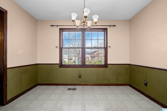 unfurnished room featuring an inviting chandelier and wooden walls