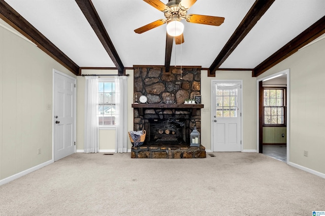 unfurnished living room featuring plenty of natural light, carpet floors, beam ceiling, and a stone fireplace