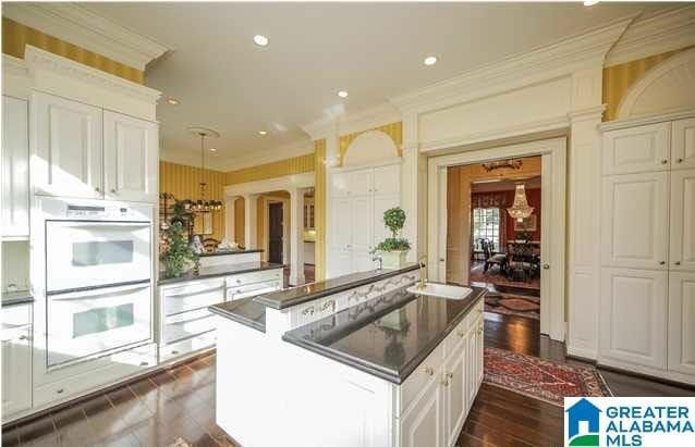 kitchen featuring double oven, white cabinetry, a kitchen island, dark hardwood / wood-style flooring, and ornamental molding