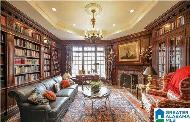 sitting room with a fireplace, a notable chandelier, ornamental molding, a raised ceiling, and built in features