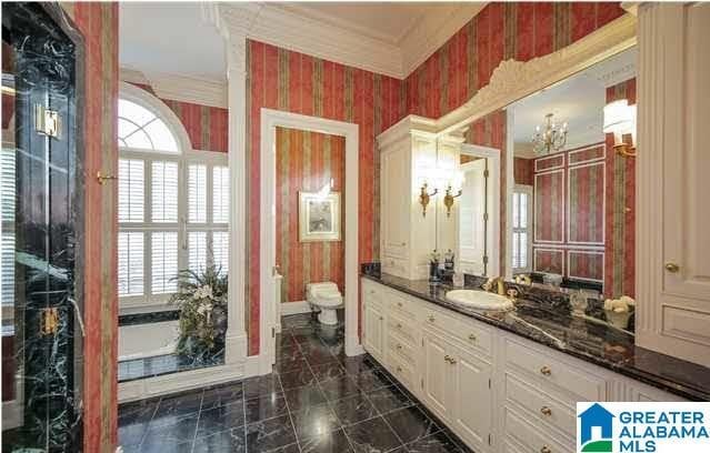 bathroom with toilet, a chandelier, a bathing tub, ornamental molding, and vanity