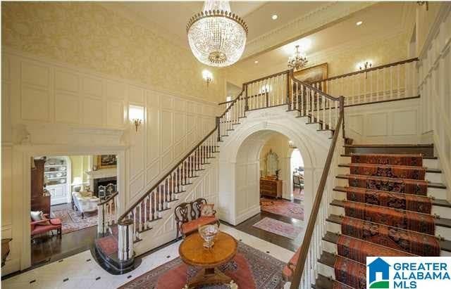 stairway with arched walkways, a fireplace, a high ceiling, ornamental molding, and a chandelier