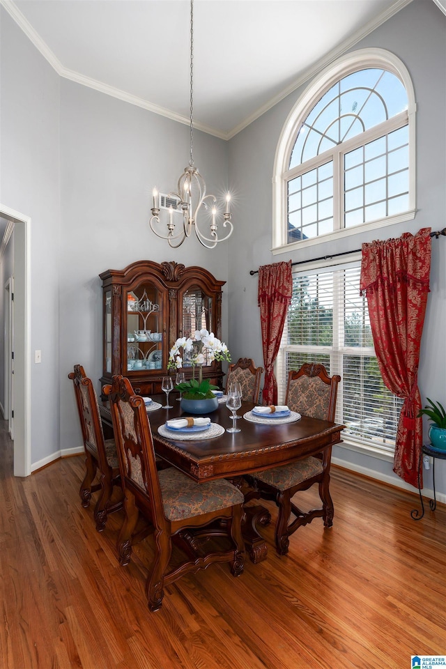 dining area featuring wood-type flooring, a chandelier, crown molding, and a towering ceiling