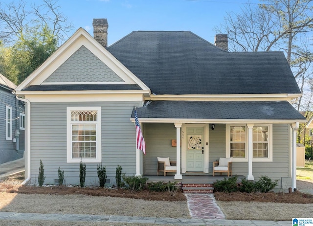 view of front of home with crawl space, covered porch, a shingled roof, and a chimney