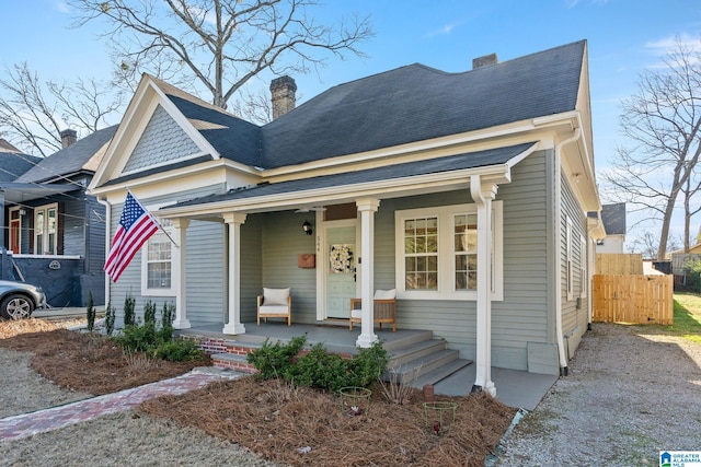 view of front of property with a shingled roof, covered porch, fence, and a chimney