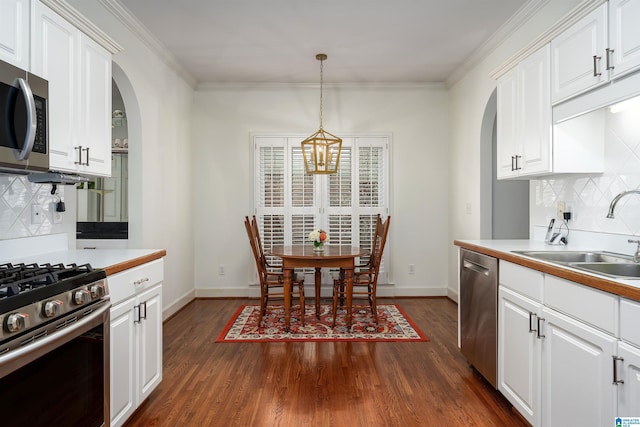 kitchen featuring arched walkways, decorative light fixtures, stainless steel appliances, white cabinets, and a sink