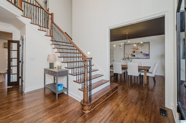 staircase with a towering ceiling, wood finished floors, visible vents, and baseboards