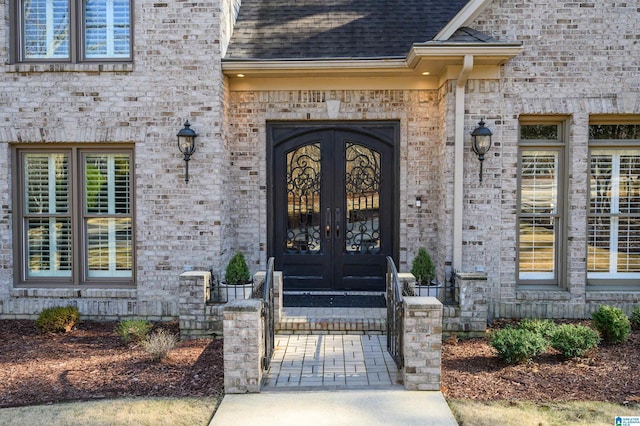 entrance to property with brick siding, a shingled roof, and french doors