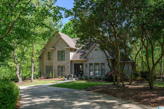 view of front facade featuring brick siding, a front yard, and roof with shingles