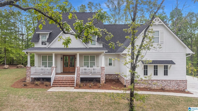 view of front of home with a porch, french doors, a shingled roof, and a front lawn