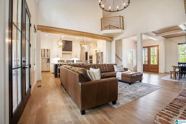 living area with light wood-type flooring, a towering ceiling, beam ceiling, and a notable chandelier