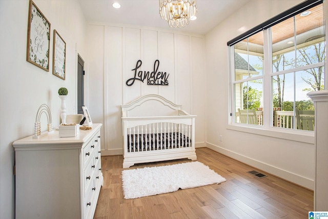 bedroom with visible vents, baseboards, a nursery area, light wood finished floors, and an inviting chandelier