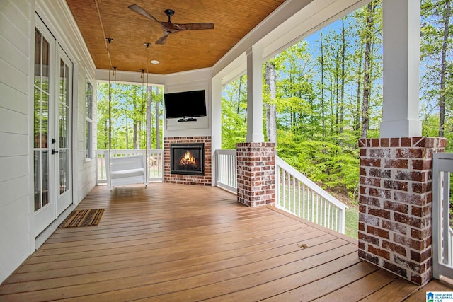 deck with an outdoor brick fireplace, ceiling fan, and french doors