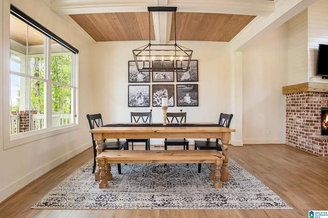 dining space with a chandelier, a brick fireplace, beam ceiling, and wood finished floors