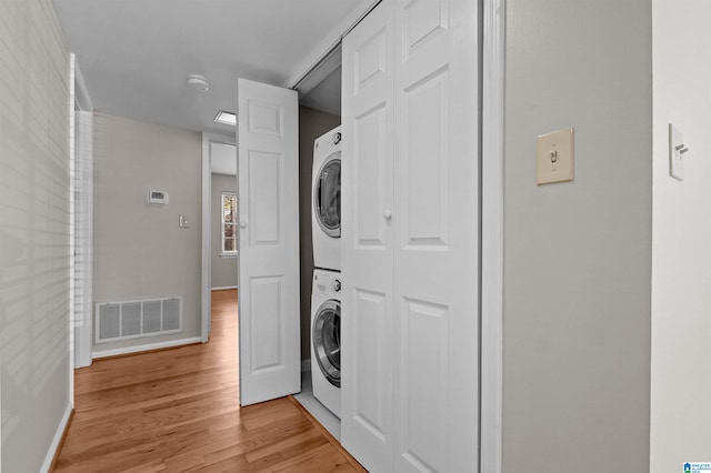 washroom with stacked washer / drying machine and light hardwood / wood-style flooring