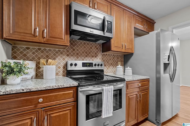 kitchen with decorative backsplash, light hardwood / wood-style floors, stainless steel appliances, and light stone counters