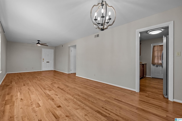 empty room with ceiling fan with notable chandelier and light wood-type flooring