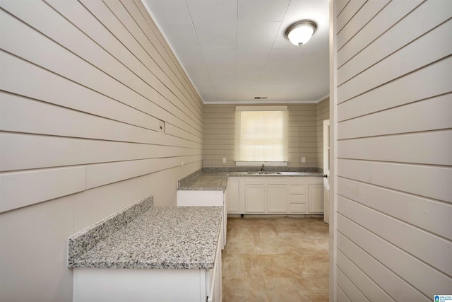 kitchen with sink, wood walls, white cabinets, and light stone countertops