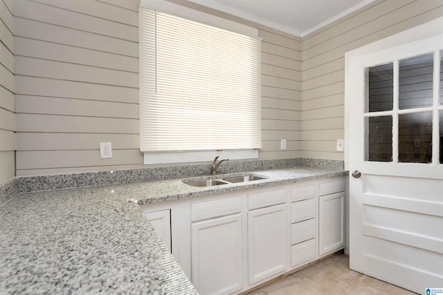 kitchen featuring wood walls, white cabinetry, sink, and light stone counters