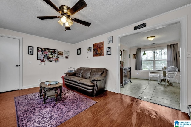 living area featuring a textured ceiling, wood finished floors, a ceiling fan, and baseboards