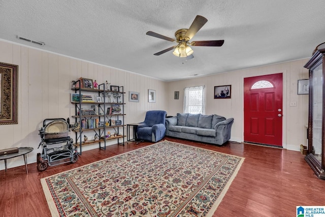 living area featuring a ceiling fan, dark wood-style flooring, visible vents, and a textured ceiling