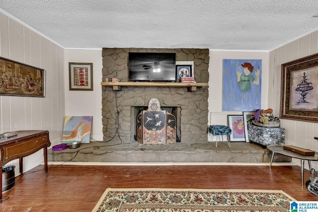 living area with a textured ceiling, ornamental molding, wood finished floors, and a stone fireplace