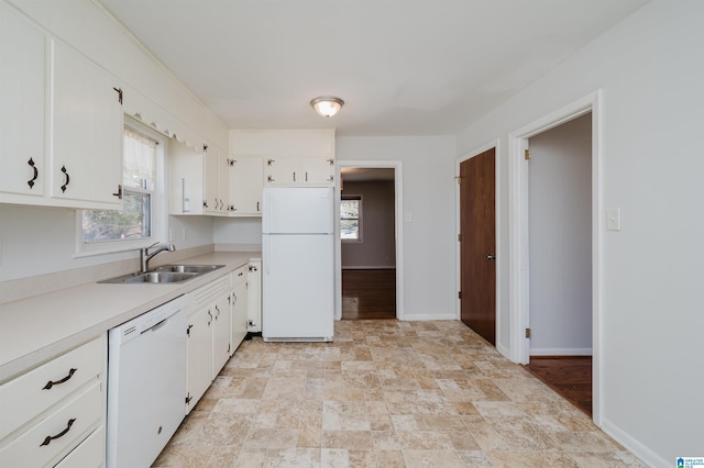 kitchen featuring white appliances, a sink, white cabinets, light countertops, and plenty of natural light