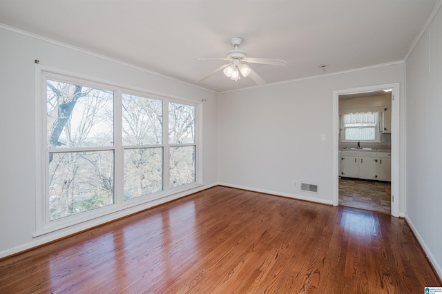 spare room with a sink, a ceiling fan, wood finished floors, visible vents, and crown molding