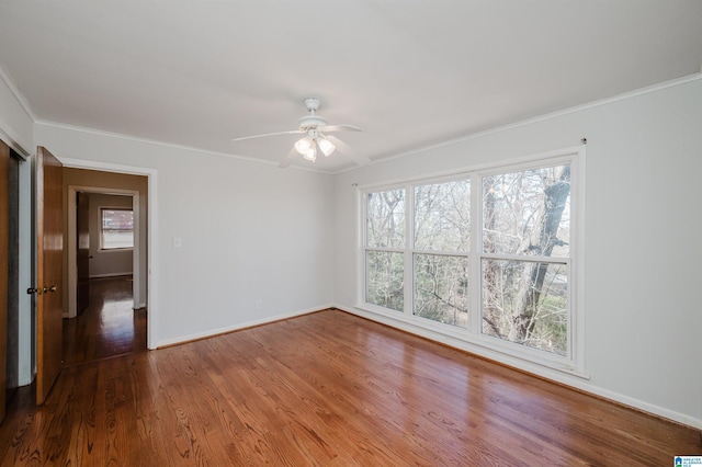 empty room with baseboards, plenty of natural light, wood finished floors, and crown molding