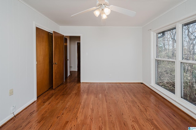 spare room with a ceiling fan, crown molding, baseboards, and wood finished floors