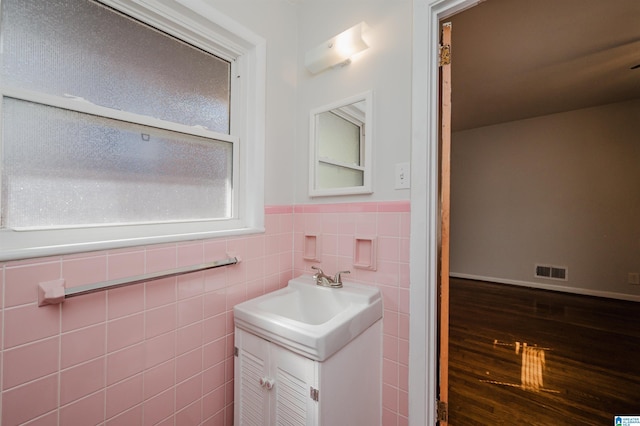 bathroom with a wainscoted wall, wood finished floors, vanity, visible vents, and tile walls