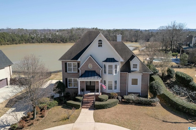 view of front of house featuring a water view, brick siding, a chimney, and stucco siding