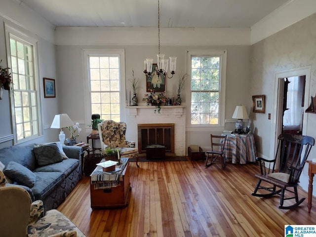 sitting room featuring a wealth of natural light, a brick fireplace, a notable chandelier, and wood finished floors