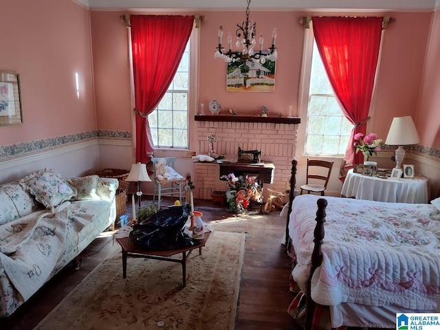 bedroom featuring a brick fireplace, multiple windows, a chandelier, and dark wood-style flooring