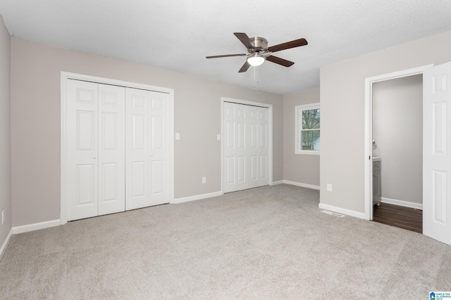 unfurnished bedroom featuring light carpet, ceiling fan, a textured ceiling, and two closets