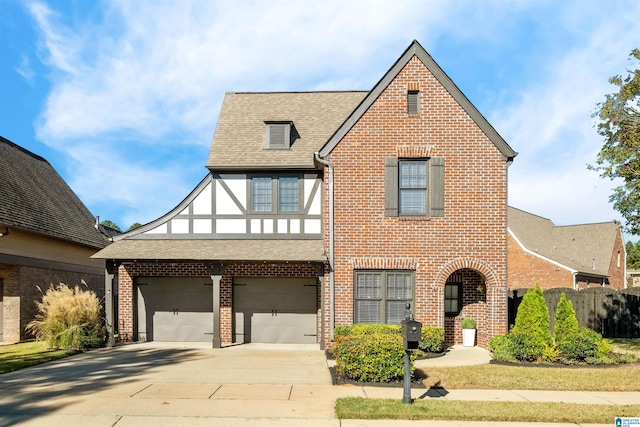 tudor home with a shingled roof, concrete driveway, and brick siding