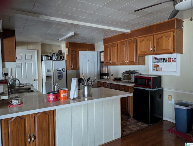 kitchen with sink, white fridge with ice dispenser, black refrigerator, and kitchen peninsula