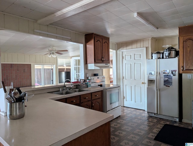 kitchen with sink, white appliances, wooden walls, and ceiling fan