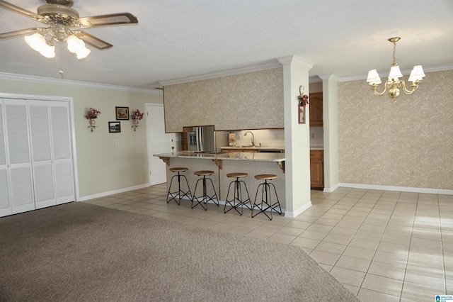 kitchen with light tile patterned floors, stainless steel fridge with ice dispenser, ceiling fan with notable chandelier, a breakfast bar area, and ornamental molding