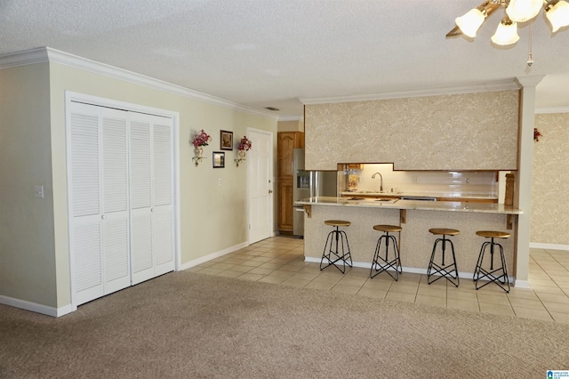 kitchen with stainless steel refrigerator with ice dispenser, light carpet, ornamental molding, a kitchen bar, and kitchen peninsula