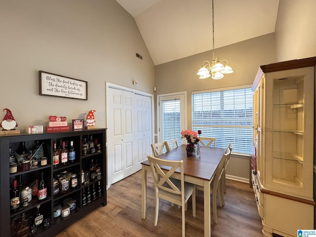 dining area with high vaulted ceiling, a healthy amount of sunlight, a chandelier, and wood-type flooring