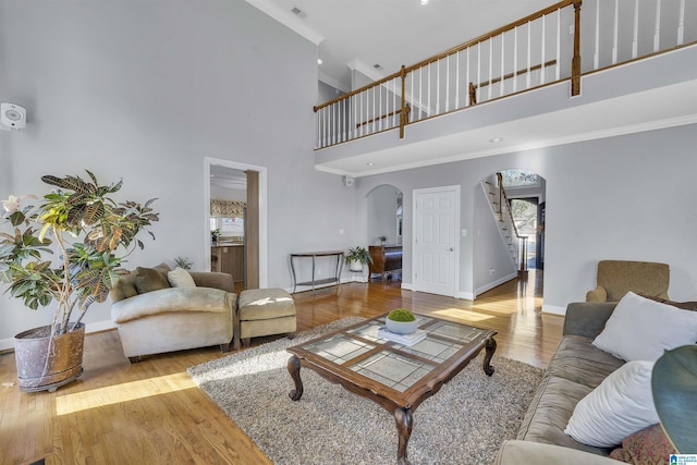 living area with arched walkways, baseboards, light wood-style floors, stairway, and crown molding