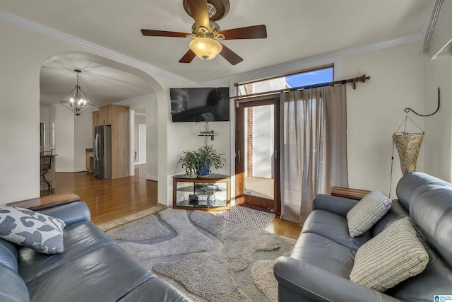 living room featuring arched walkways, ornamental molding, ceiling fan with notable chandelier, and light wood-style flooring