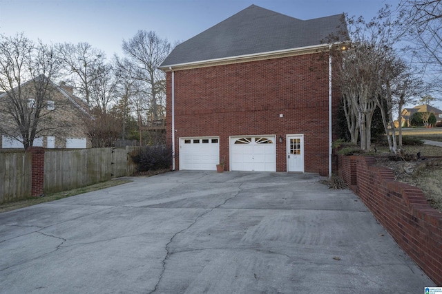 view of property exterior featuring driveway, an attached garage, fence, and brick siding