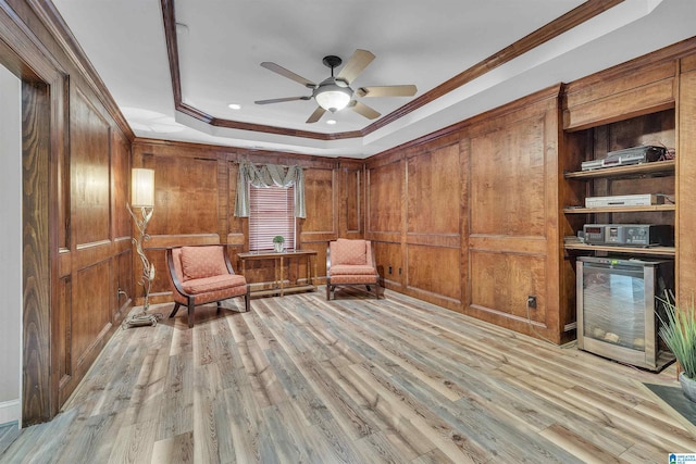 living area featuring ornamental molding, a tray ceiling, wood walls, and light wood-style flooring